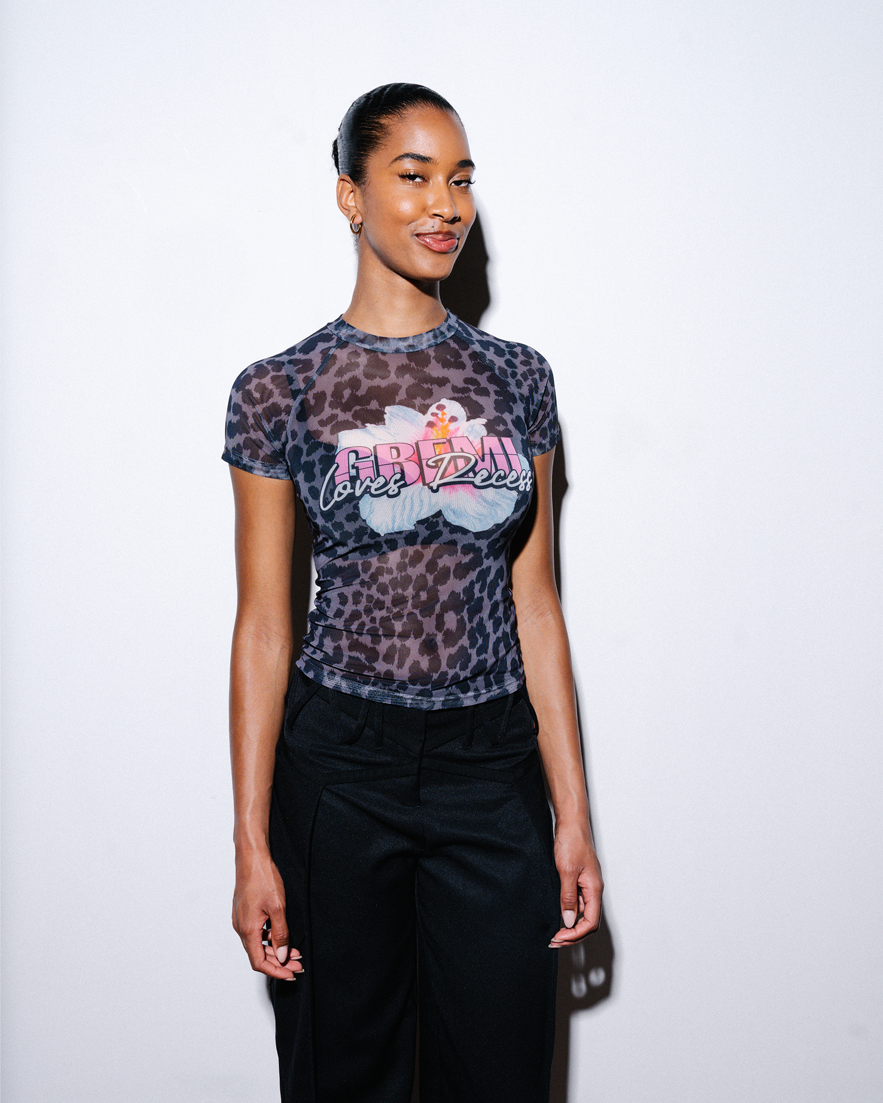 Model wearing a black leopard print t-shirt with graphic design and text which reads "Gbemi loves Recess", standing against a plain background.